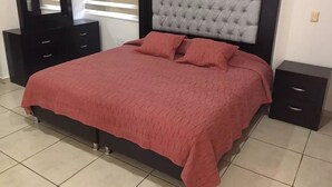 A bedroom with a bed, nightstands, a dresser, and a window with blinds.