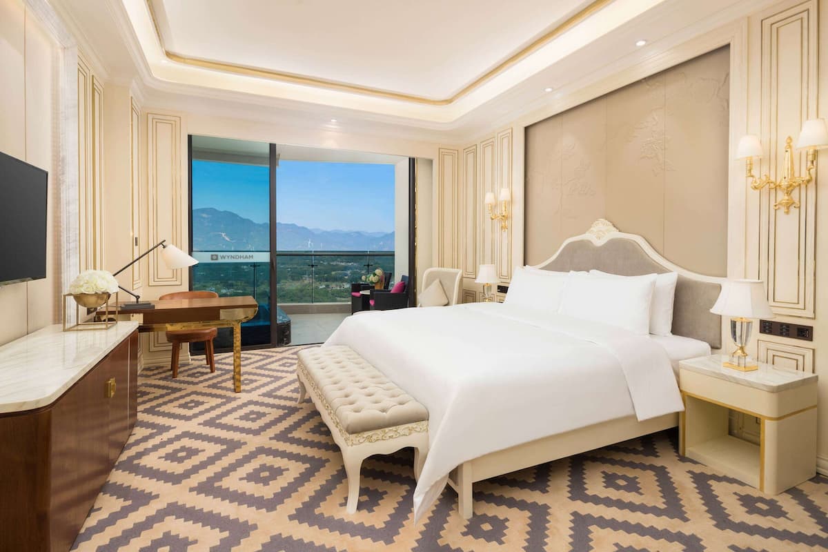 A hotel room with a large bed, a desk, a chair, a bench, and a TV.