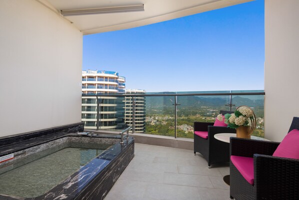 A balcony with a hot tub, wicker furniture, and a view of city buildings. - Wyndham Nankunshan (Huizhou)