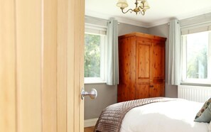 A bedroom with a wooden wardrobe, a bed with a white duvet, and a window with curtains.