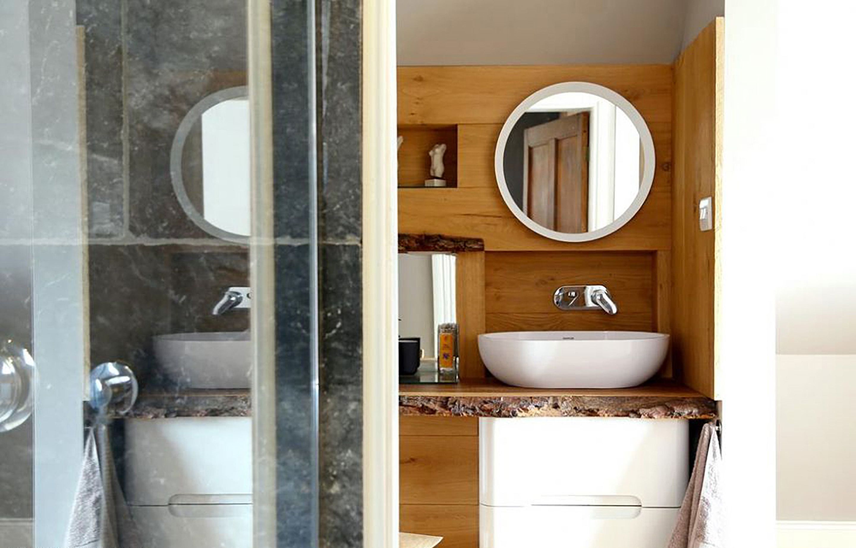 A bathroom with a marble shower, a white sink, and wooden cabinetry.
