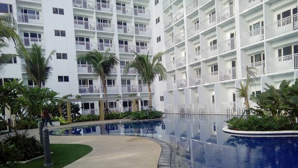 A modern hotel with multiple balconies, a central pool area, and surrounding greenery. - Francisco Place (Pasay)