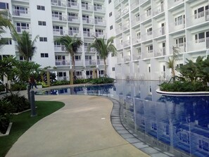 Un hôtel moderne doté de nombreux balcons, d’un espace piscine central et d’un environnement verdoyant.