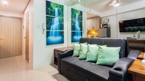 A modern living room with a black leather sofa, a wooden side table, and a flat-screen TV mounted on the wall. - Francisco Place (Pasay)