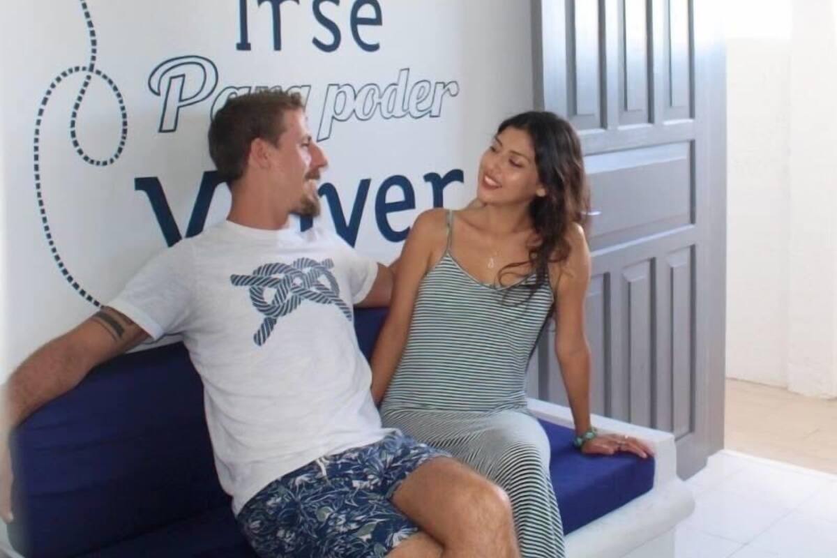 Un couple est assis sur un canapé bleu dans une chambre d’hôtel moderne. Un mur porte une citation inspirante.