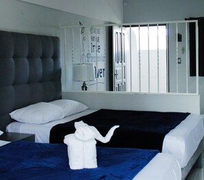 Hotelkamer met twee bedden, een groot gestoffeerd hoofdeinde, een raam met tralies en een handdoek op het bed.