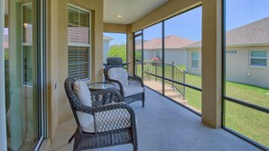 A covered patio with wicker chairs, a grill, and a view of neighboring houses. - BEAUTIFUL HOME GAS GOLF CART NEAR BROWNWOOD PADDOCK SQ    THE VILLAGES FL (The Villages)