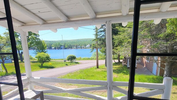 A room with a view of a lake and greenery, a window with blinds, and a table with a tray and a book. - Eagle Harbor- Harbor View: Soak Up the Sun at a Beachside Cottage This Summer (Eagle Harbor)