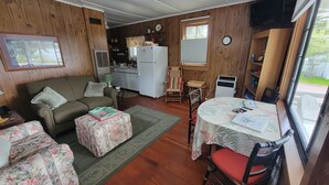 A cozy living room with a sofa, a coffee table, and a dining table with chairs. There is a kitchen area with a refrigerator, stove, and sink. - Eagle Harbor- Harbor View: Soak Up the Sun at a Beachside Cottage This Summer (Eagle Harbor)