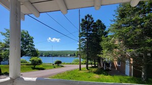 A covered porch with a view of a lake, surrounded by trees and a building with a brick exterior. - Eagle Harbor- Harbor View: Soak Up the Sun at a Beachside Cottage This Summer (Eagle Harbor)