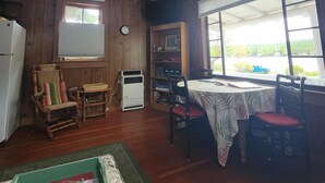 A room with wooden walls, a dining table with chairs, a small refrigerator, a clock, and a window with a view of the outside. - Eagle Harbor- Harbor View: Soak Up the Sun at a Beachside Cottage This Summer (Eagle Harbor)