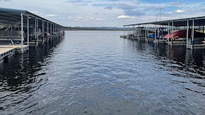 Un port de plaisance où les bateaux sont amarrés sous des structures abritées, l’eau est calme et le ciel est dégagé.