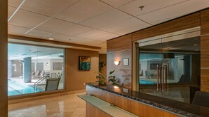 Un espace d’accueil doté d’une cloison en verre, d’un comptoir de réception en bois et offrant une vue sur la zone de la piscine.