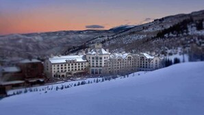 Un grand hôtel à plusieurs étages, doté d’une façade symétrique, entouré de montagnes enneigées et surplombant un ciel dégagé.