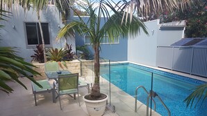 A swimming pool with a glass barrier, a palm tree, and a table with chairs. - Beautiful Beach-side cottage with lap pool in North Maroubra close to Coogee (Maroubra)