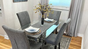 Una mesa de comedor con cuatro sillas tapizadas grises, un tablero de vidrio y un jarrón con flores amarillas.