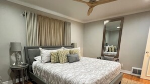 Un dormitorio moderno con una cama grande, ventilador de techo, espejo y mesita de noche con lámpara.