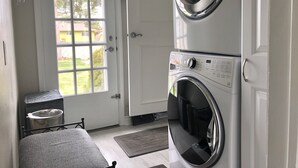 Un cuarto de lavandería con lavadora y secadora de carga frontal, una puerta con ventana y un pequeño cubo de basura.