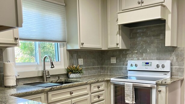 Una cocina con gabinetes blancos, encimera de granito, pileta de acero inoxidable y estufa blanca.