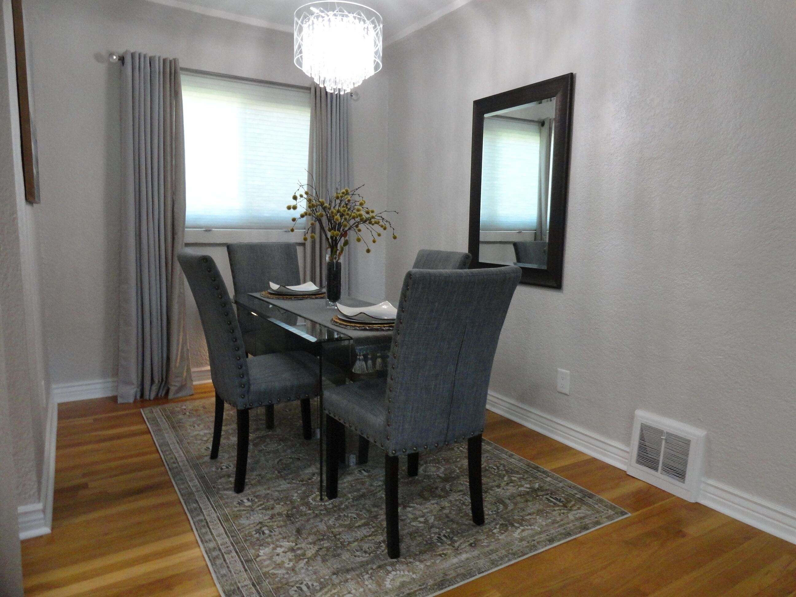 A dining area with a table, chairs, a vase with flowers, a chandelier, and a mirror on the wall.