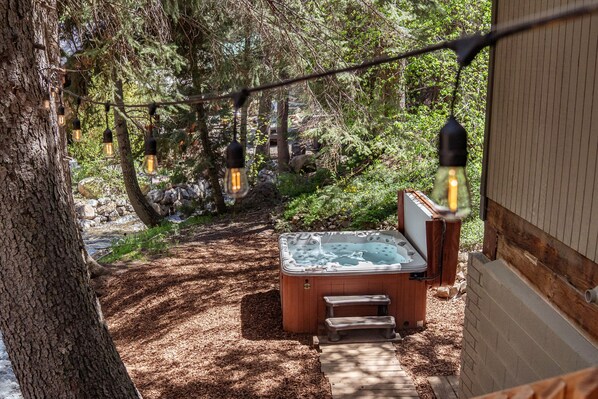 A hot tub with a wooden bench, surrounded by trees and a wooden deck.