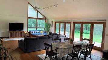 Un salon spacieux avec une grande télévision, un ensemble de canapés, une table à manger avec des chaises et un ventilateur de plafond.