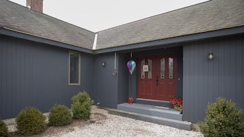 Une maison à deux étages, à l’extérieur de couleur gris foncé, avec une porte d’entrée rouge et un petit porche agrémenté d’un panier rempli de fleurs rouges.