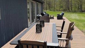 An outdoor patio with a long table and multiple chairs, a barbecue grill, and a view of a grassy area with trees. - Spacious Home nestled along the Blackberry River in Northwest CT (East Canaan)