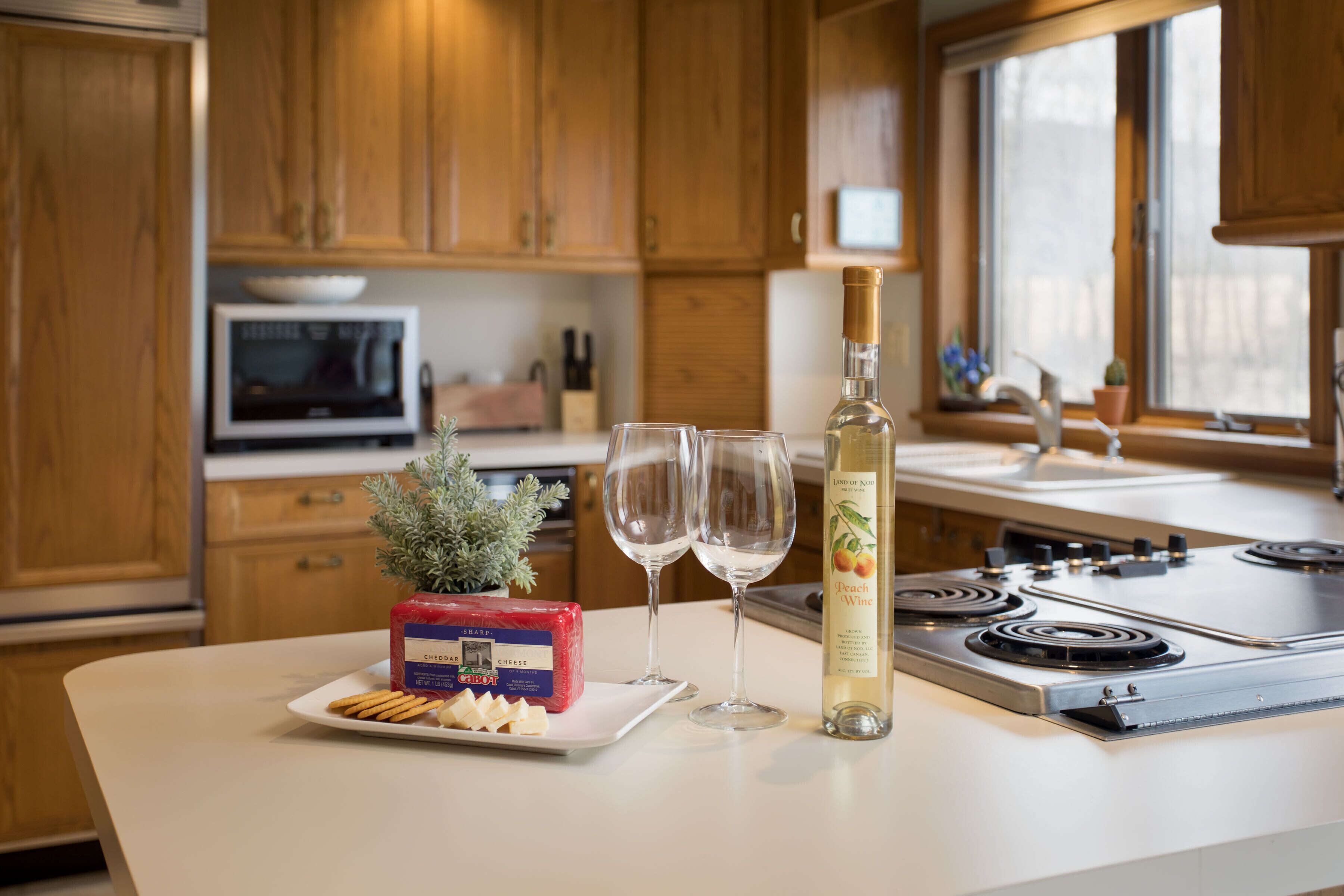 Une cuisine avec des meubles en bois, un four à micro-ondes, une cuisinière et une bouteille de vin à la pêche.