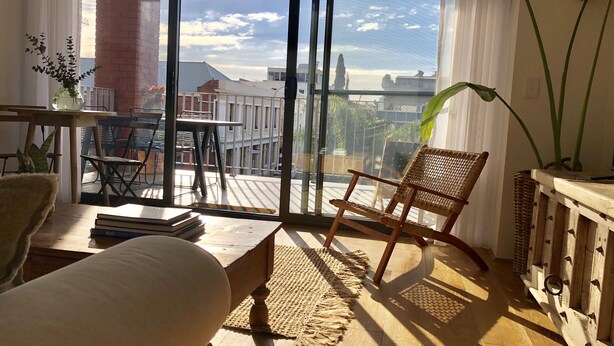 A cozy room with a large window, a wooden chair, a small table, and a sofa. - New apartment in the historic West End close to cafes bars and restaurants.  (Fremantle)