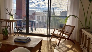 A spacious room with a large sliding glass door leading to an outdoor balcony, a wooden table with books, a wicker chair, and a potted plant. - New apartment in the historic West End close to cafes bars and restaurants.  (Fremantle)