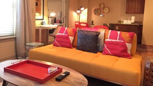 Ein Wohnzimmer mit einem gelben Sofa, roten und schwarzen Kissen, einem roten Tablett und einer Fernbedienung.