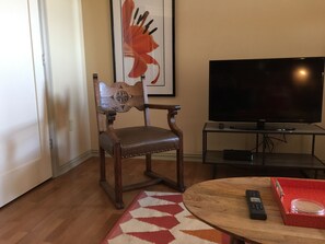 Un salon avec un fauteuil en bois, un téléviseur posé sur un meuble, une table basse ronde et une boîte rouge.