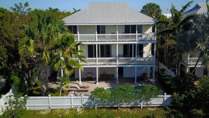 A two-story house with a balcony on the second floor, surrounded by palm trees and a white picket fence. - Waterfront Home in Key Cove Landings (Key West)