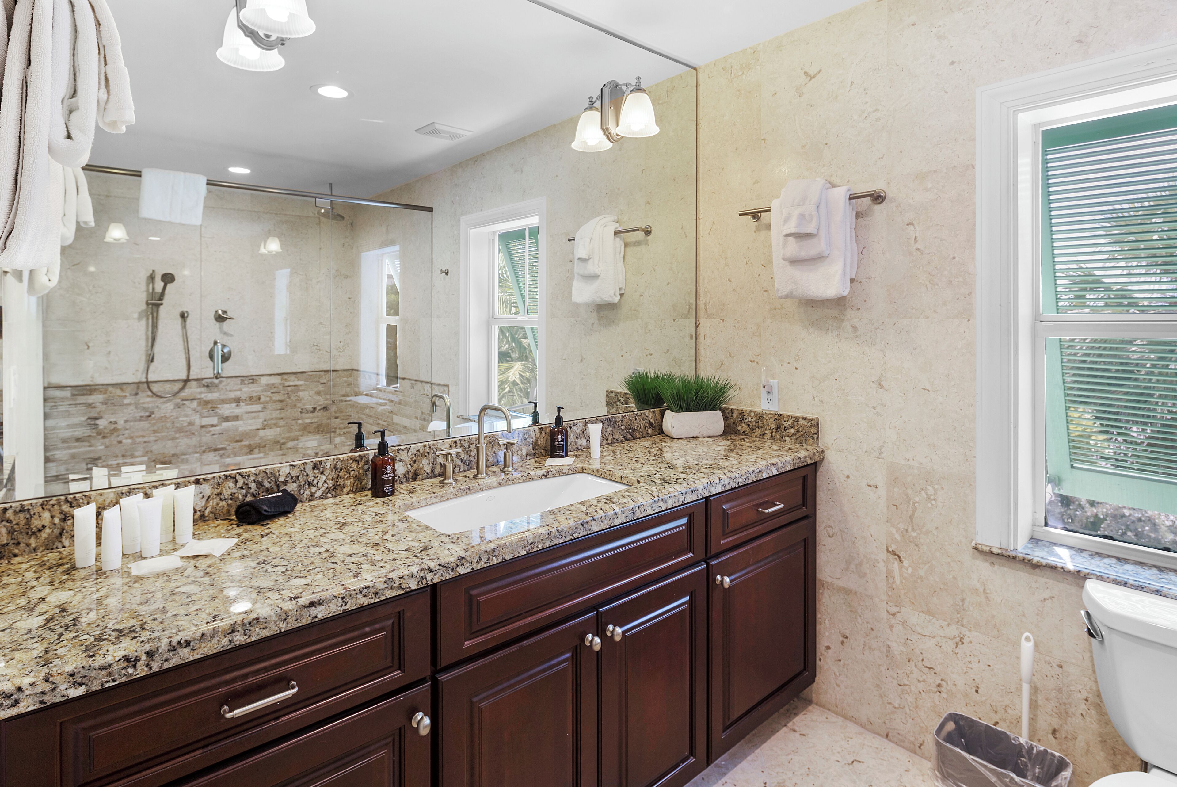 A bathroom with a granite countertop, a sink, a mirror, a shower, and a toilet.