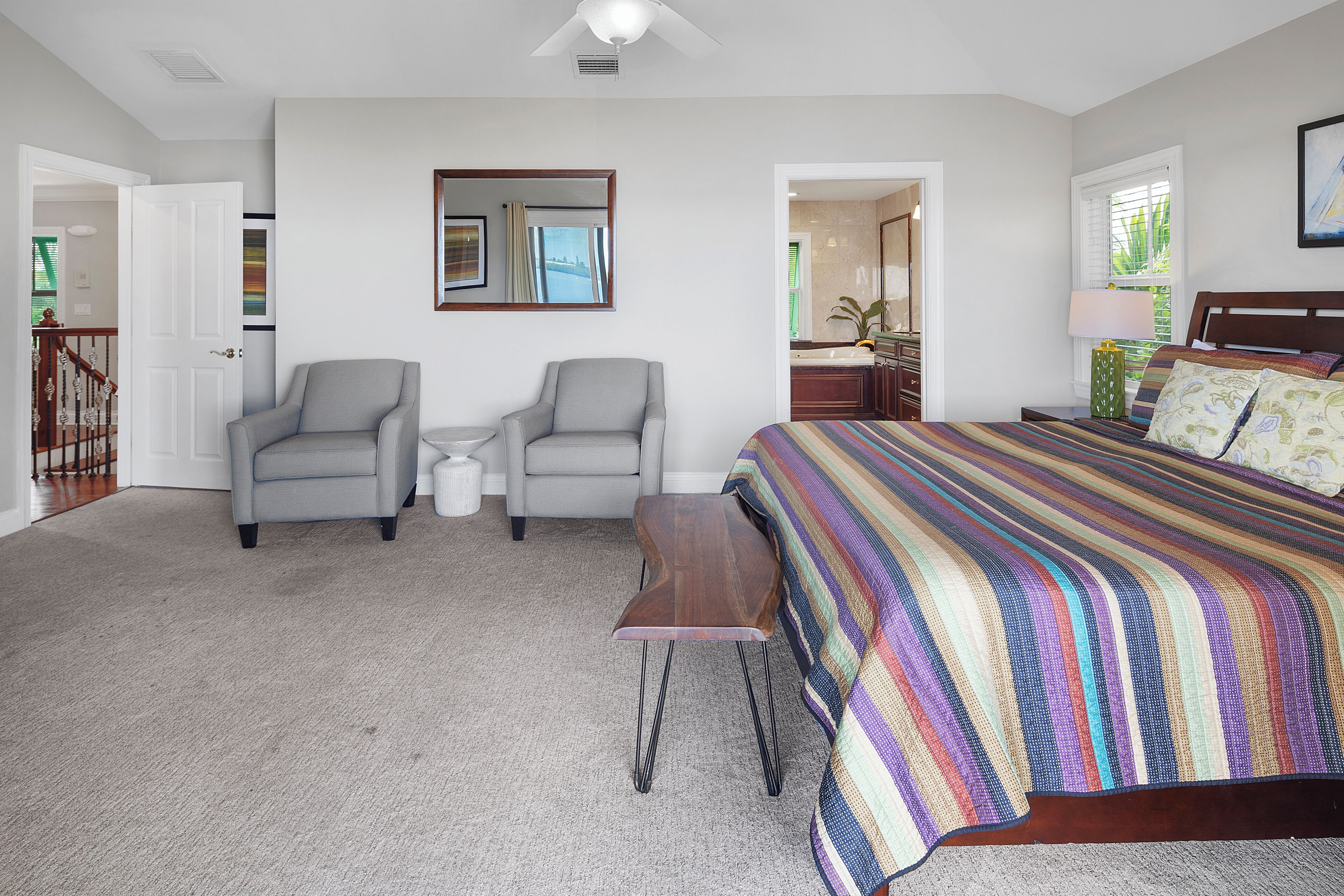 Un dormitorio con una cama, dos sillones, una mesita y vistas al baño y la cocina a través de una puerta abierta.