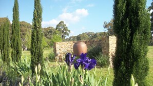 A garden with tall green shrubs, a stone wall, and a large terracotta pot. - Casina Marcella - country house (Basalt)