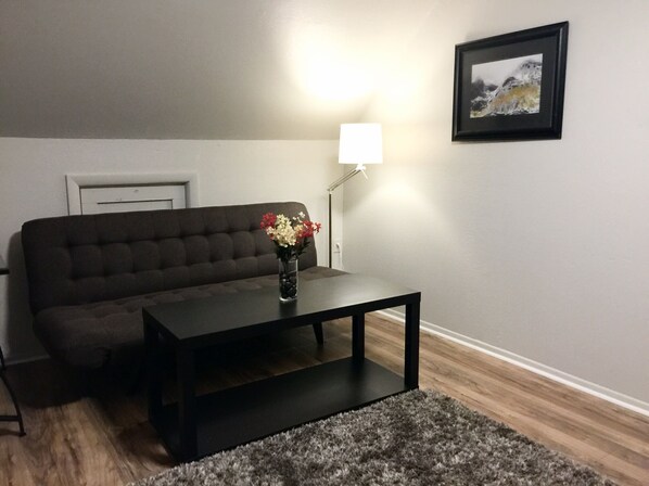 A living room with a dark sofa, a coffee table, a lamp, and a framed picture on the wall. - Loft at Red Rock ✦ Best COS Area❣ (Colorado Springs)