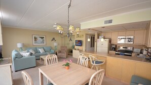 A living room with a sofa, a dining table with chairs, a kitchen area with a refrigerator, microwave, and stove.
