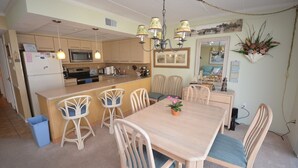 A kitchen with a central island, wooden chairs, a dining table, and a chandelier.