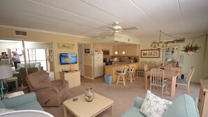A living room with a sofa, a coffee table, and a TV. There is a kitchen area with a dining table and chairs.