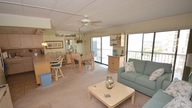 A spacious living area with a dining table, chairs, a sofa, and a kitchen in the background.