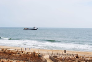 A beach with a ship in the distance, sandy shore, and a wooden fence.
