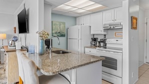 A modern kitchen with white cabinets, a granite countertop, a built-in oven, and a stainless steel refrigerator.