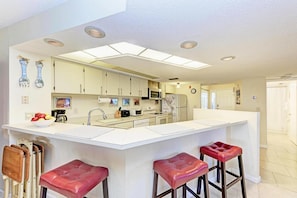 A modern kitchen with a central island, bar stools, and a microwave.