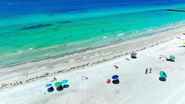 Una spiaggia con acque cristalline turchesi, una battigia sabbiosa e diversi ombrelloni.