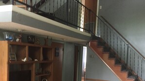 Amplia sala de estar con una escalera de madera, una estantería y una mesa de centro.