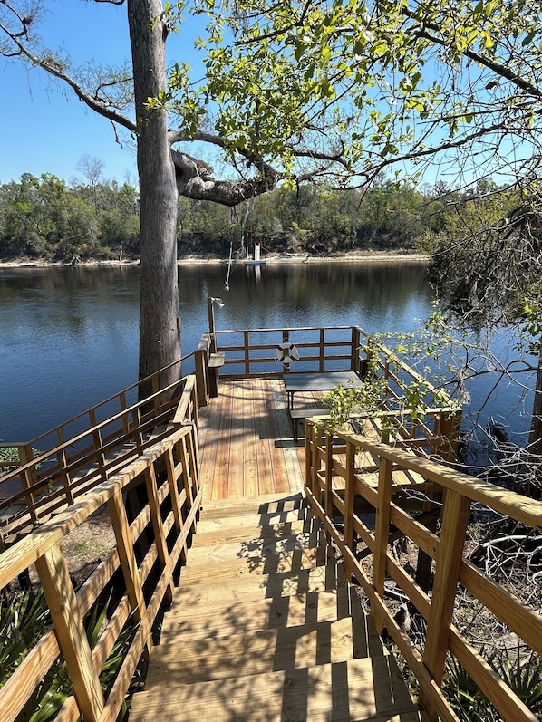 A wooden deck leading to a lake with a bench and a lifebuoy.