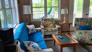 A cozy living room with a blue sofa, a floral armchair, and a wooden coffee table. - Beautiful home with wifi, tv, A/C, private dock, & backup generator power (Hope Town, Abaco)