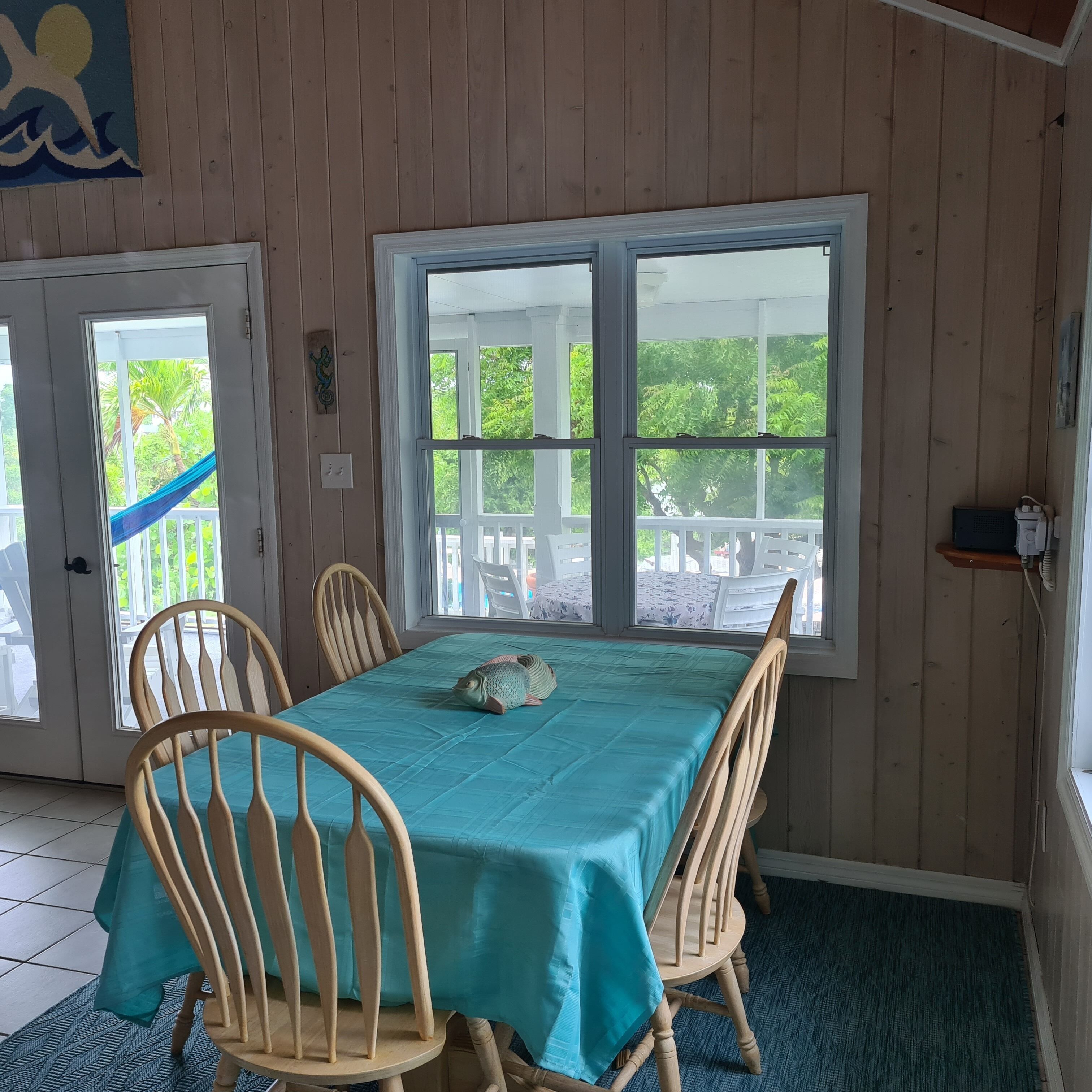 A dining area with a table covered in a teal tablecloth, surrounded by wooden chairs.